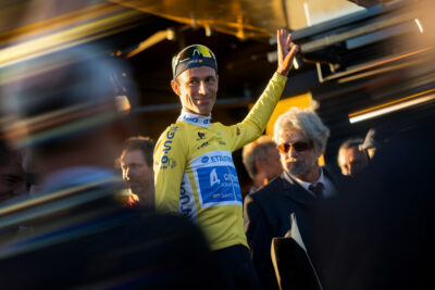 Romain Grégoire levant les bras en célébration, maillot de champion, vélo à la main.